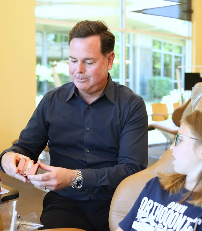 Man in dark shirt signing orthodontic documents at dental office reception desk.