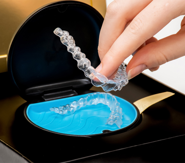 Person pouring water into blue orthodontic retainer tray over black background.