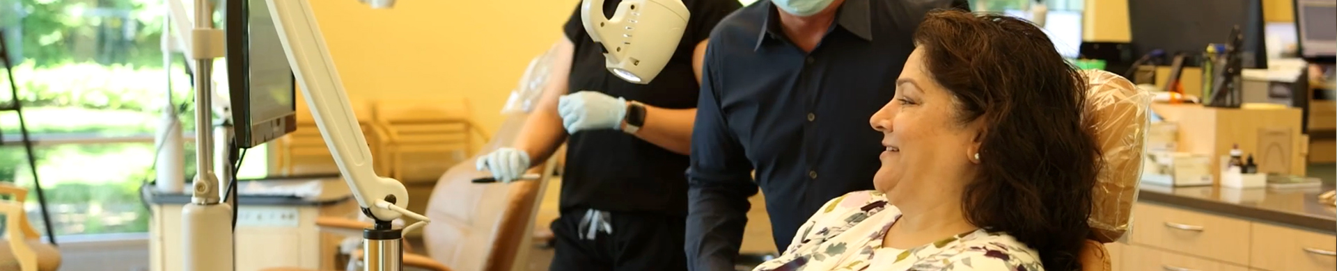 Orthodontist examining patient's teeth in modern dental office with staff present