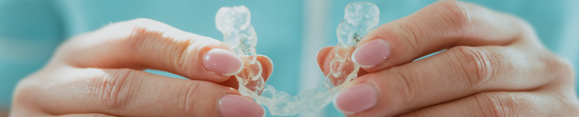 Hands holding clear orthodontic aligners against blue background, demonstrating invisible braces treatment.