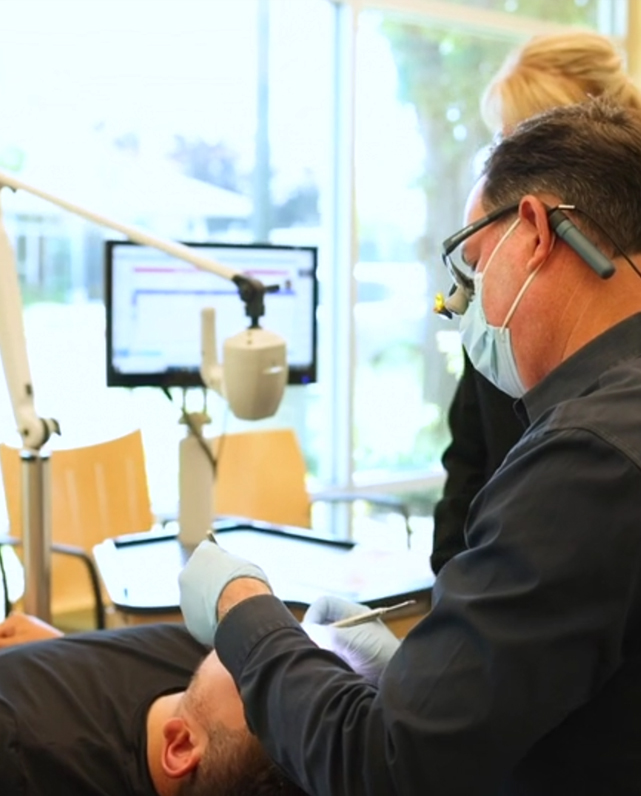 Orthodontist in mask examining patient's teeth using digital scanner in modern dental office.