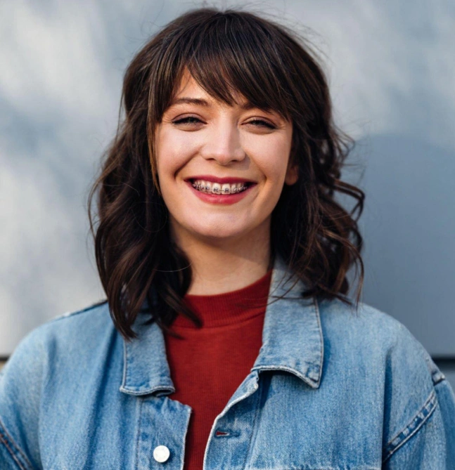 Professional headshot of smiling woman wearing denim shirt against neutral background.